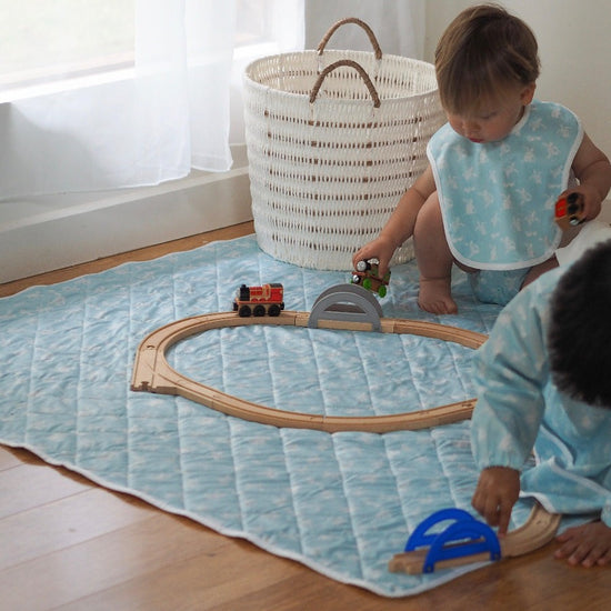 Two little boys playing trains on a mat. 