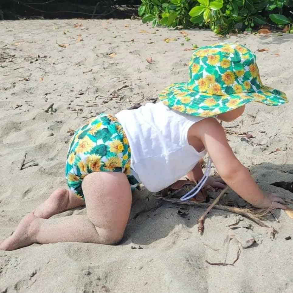 Baby crawling in sand wearing wide brim hat. 
