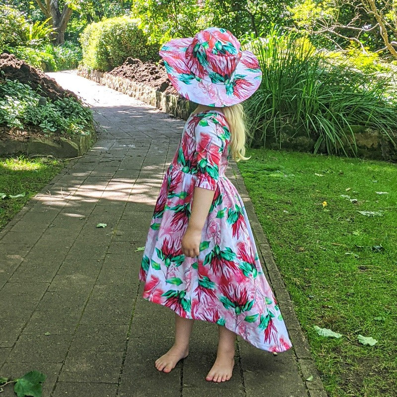 Little girl wearing matching dress and hat in garden. 