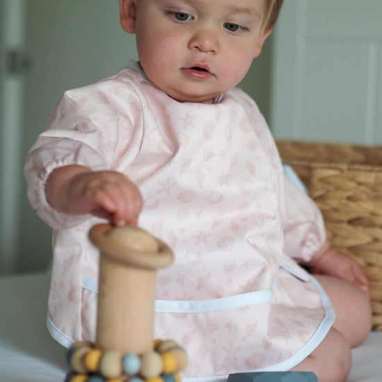 Baby playing with timber toy wearing smock