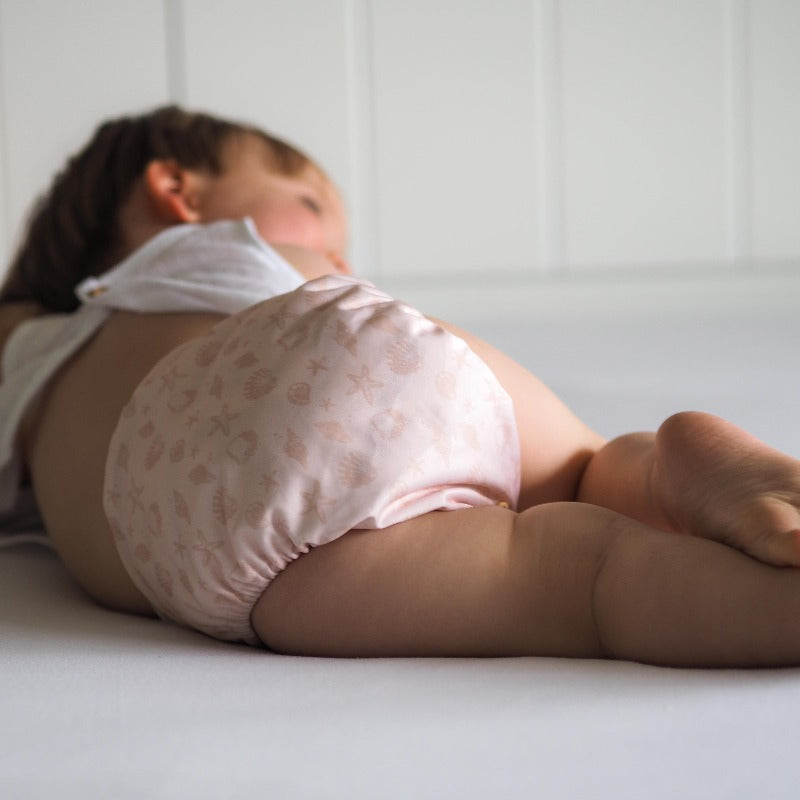 Baby laying on side wearing a reuseable cloth nappy.