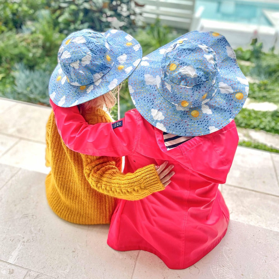 Two young children cuddling wearing matching hats. 