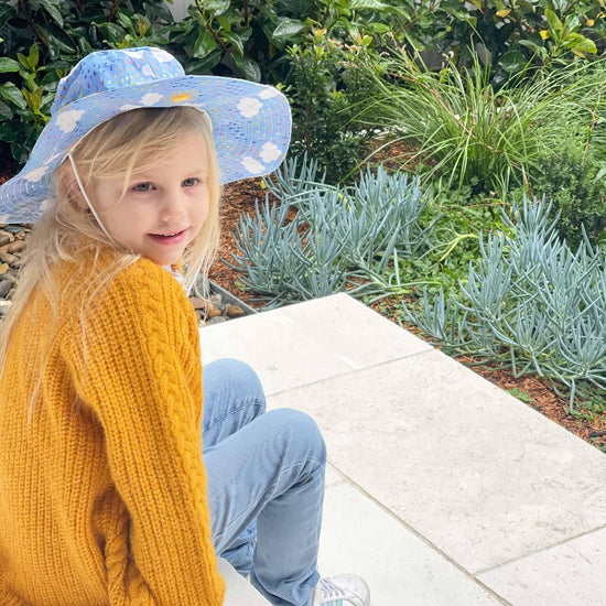 Little girl wearing hat sitting in the garden. 