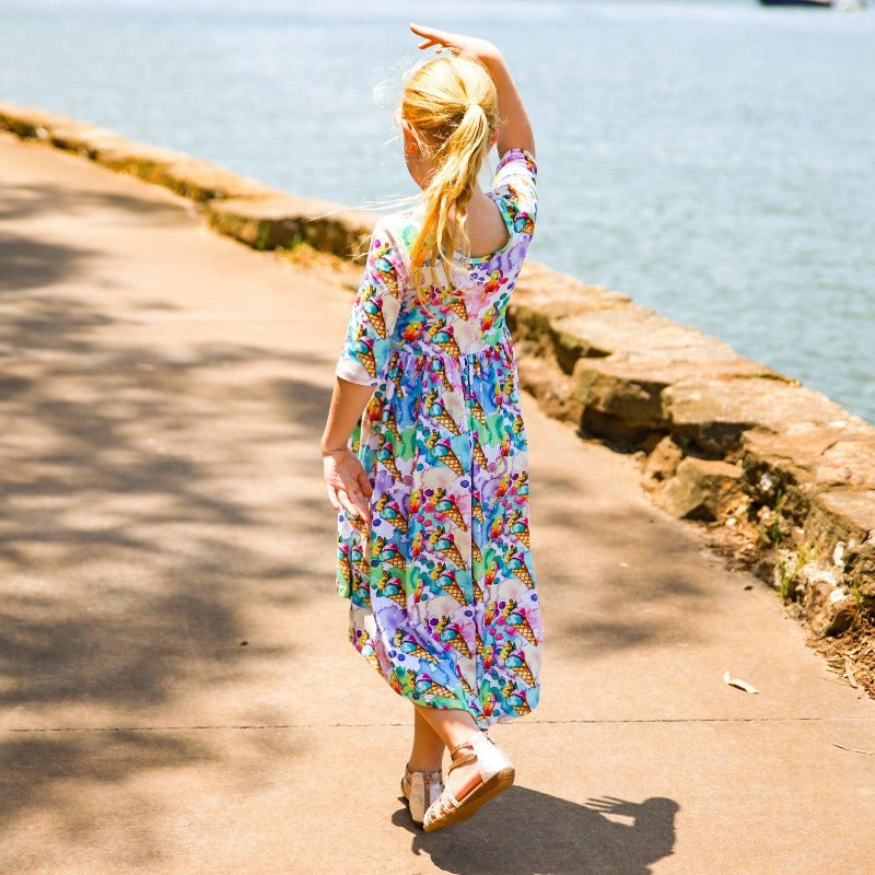 Little girl in dress walking on footpath near water.