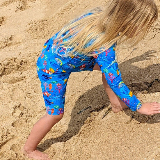 Child climbing in the sand wearing a long sleeve swimsuit