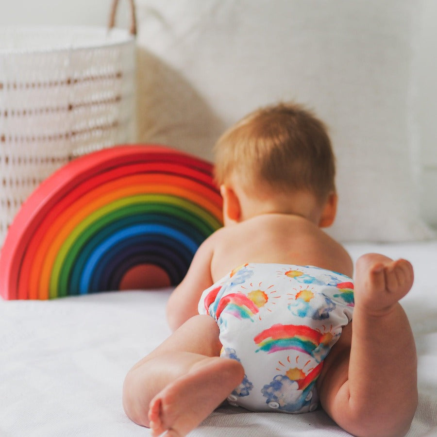 Baby wearing rainbow cloth nappy in front of rainbow timber toy