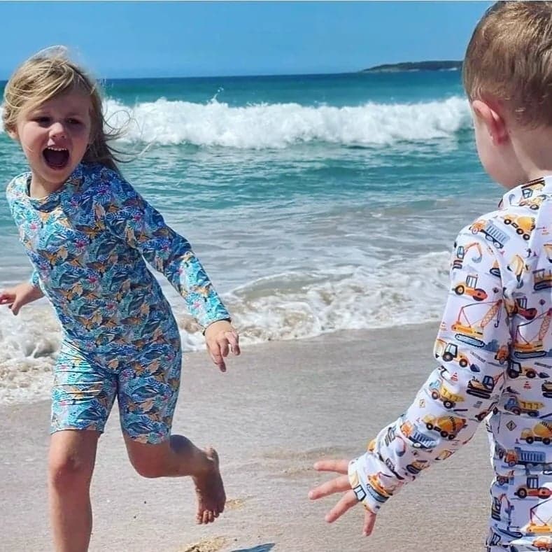 Two children playing in the surf wearing long sleeve baby bare swim wear. 