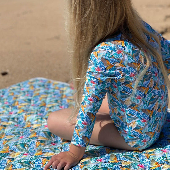 Little girl sitting on play mat at beach. 