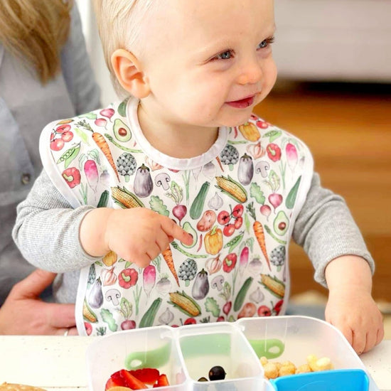 baby wearing a bib with vegetable print on the fabric