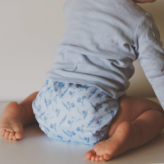 Load image into Gallery viewer, Little baby kneeling wearing a cloth nappy with a blue gumnut print. 
