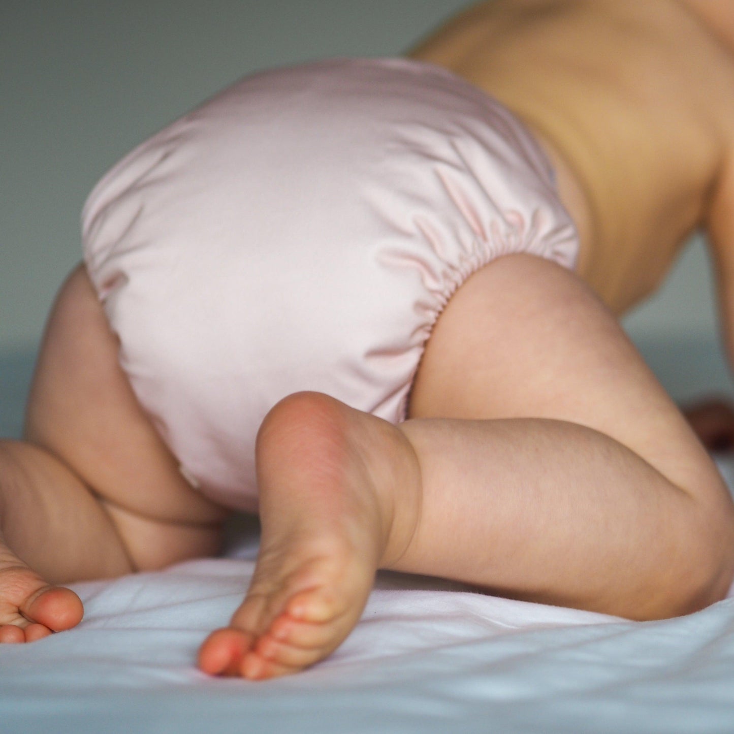 Baby crawling away wearing a blush coloured cloth nappy. 
