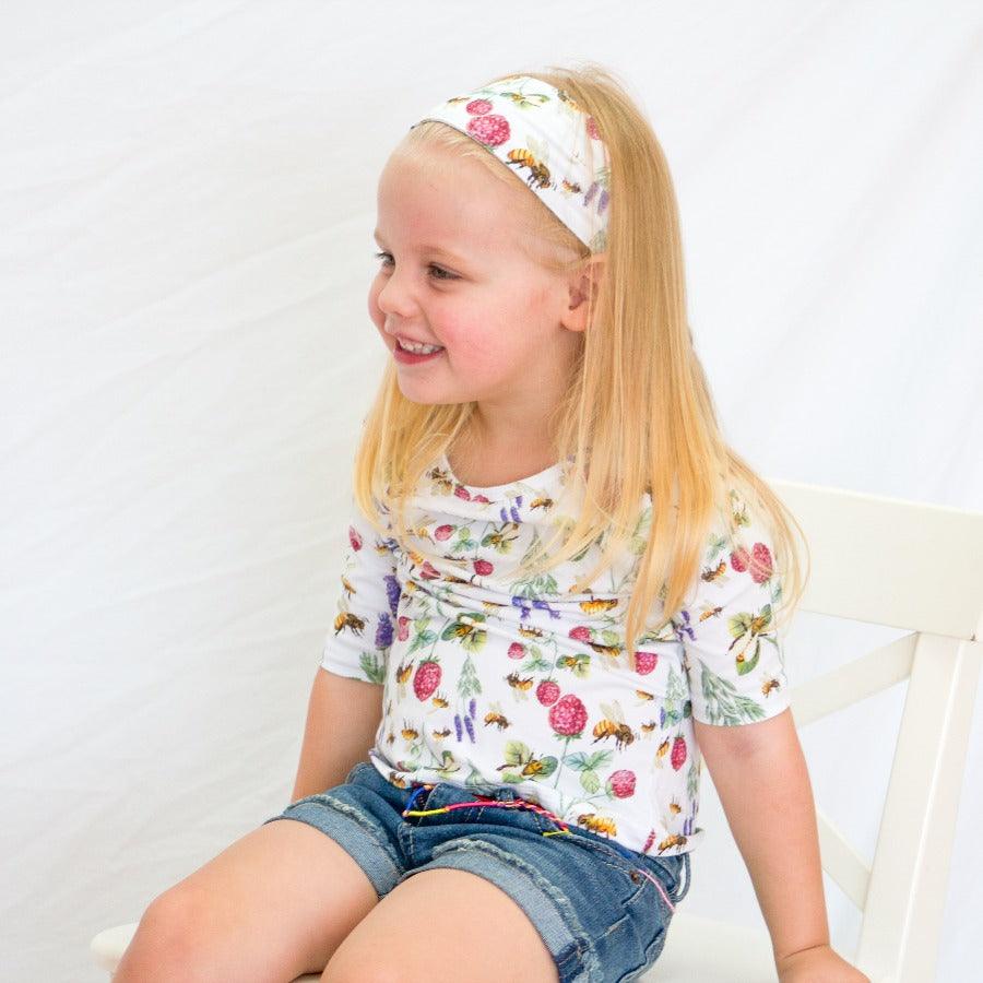 
                  
                    Little girl sitting wearing a bee print tshirt
                  
                