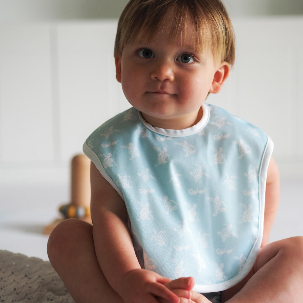 
                  
                    Baby wearing a green bib with turtle print
                  
                