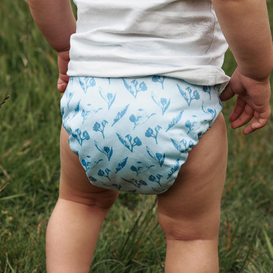 Toddler standing on grass wearing a cloth diaper. 