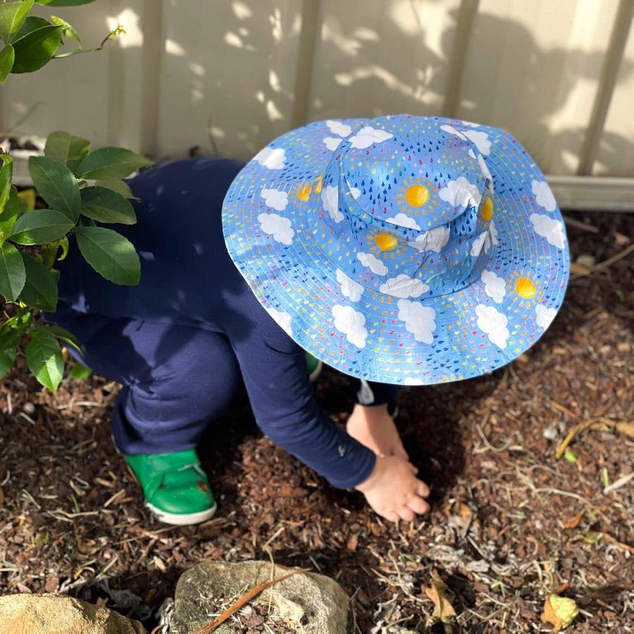 Little boy digging in garden wearing hat. 